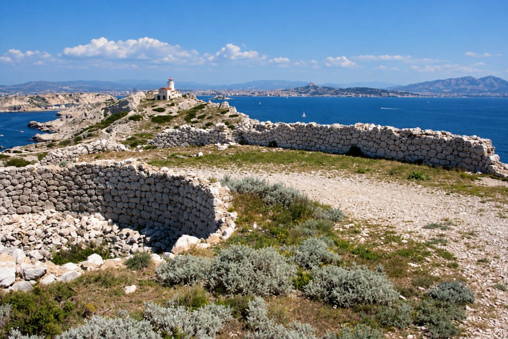 Murs circulaires en pierre sèche du fort de Cavaux dans la garrigue, phare et mer au loin