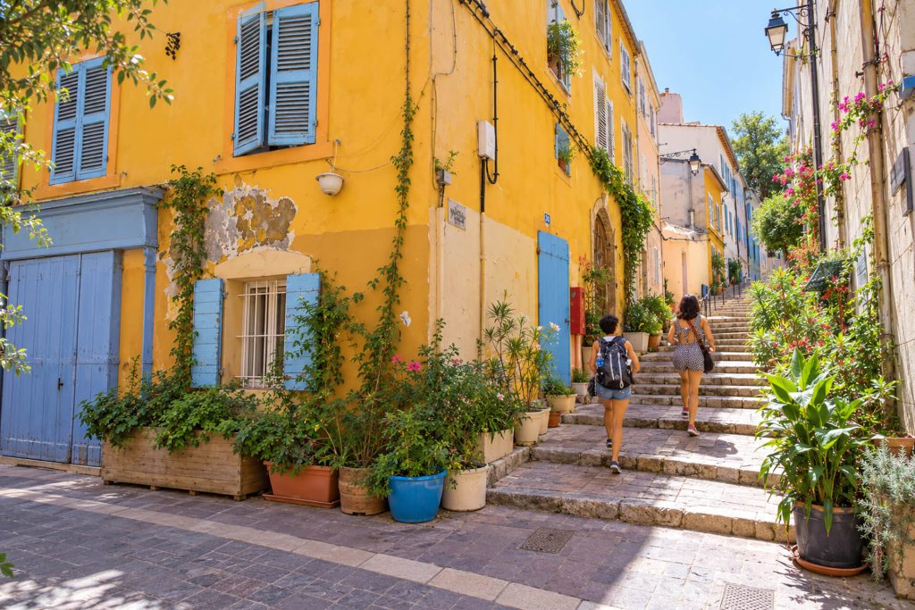 Escalier fleuri du Panier entre une façade jaune et des volets bleus, promeneurs