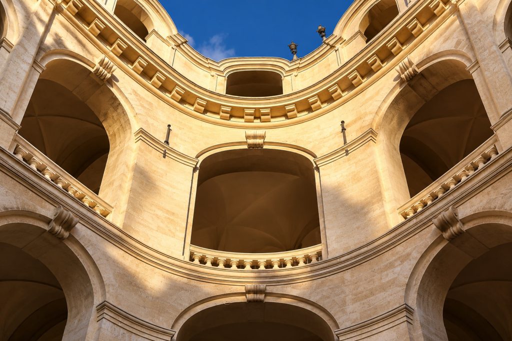 Galeries à arcades de l’Hôtel-Dieu vues d’en bas, pierre dorée et ciel bleu