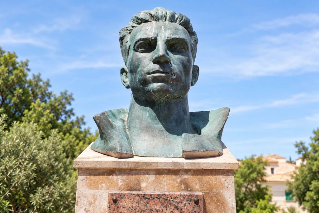 Buste en bronze de Missak Manouchian sur son socle, arbres et ciel bleu